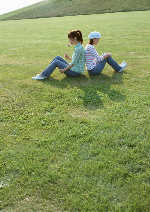 背靠背坐在草地上的两美女图片